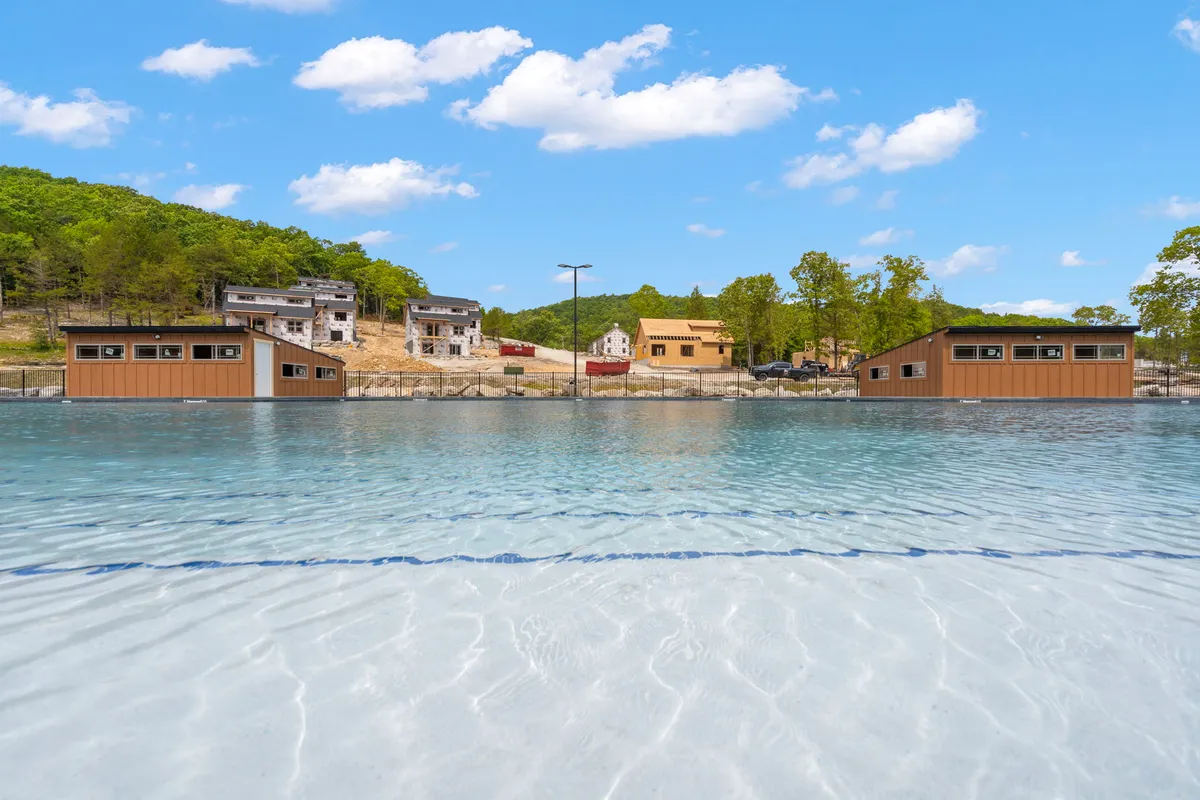A tranquil lake bordered by clear water, wooden cabins, and green hills. The scene is peaceful, ideal for fishing, swimming, or relaxing by the water in the evening with family.