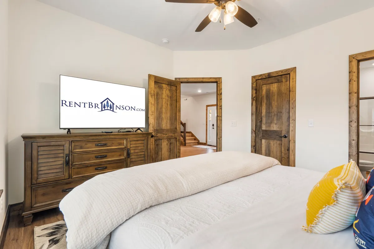 A cozy king bedroom featuring a plush bed, a wall-mounted TV, a dresser, and a door leading to an ensuite bathroom. Natural light filters in, creating a restful and inviting atmosphere, perfect for unwinding after a day of exploration.