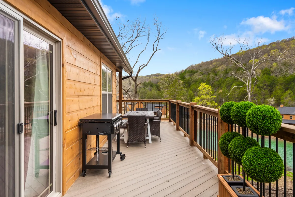 An exterior view of a well-appointed outdoor dining set and grill on a deck, flanked by topiary plants and set to a backdrop of sunset-lit skies. The environment promises enjoyable meals and relaxing evenings outdoors.