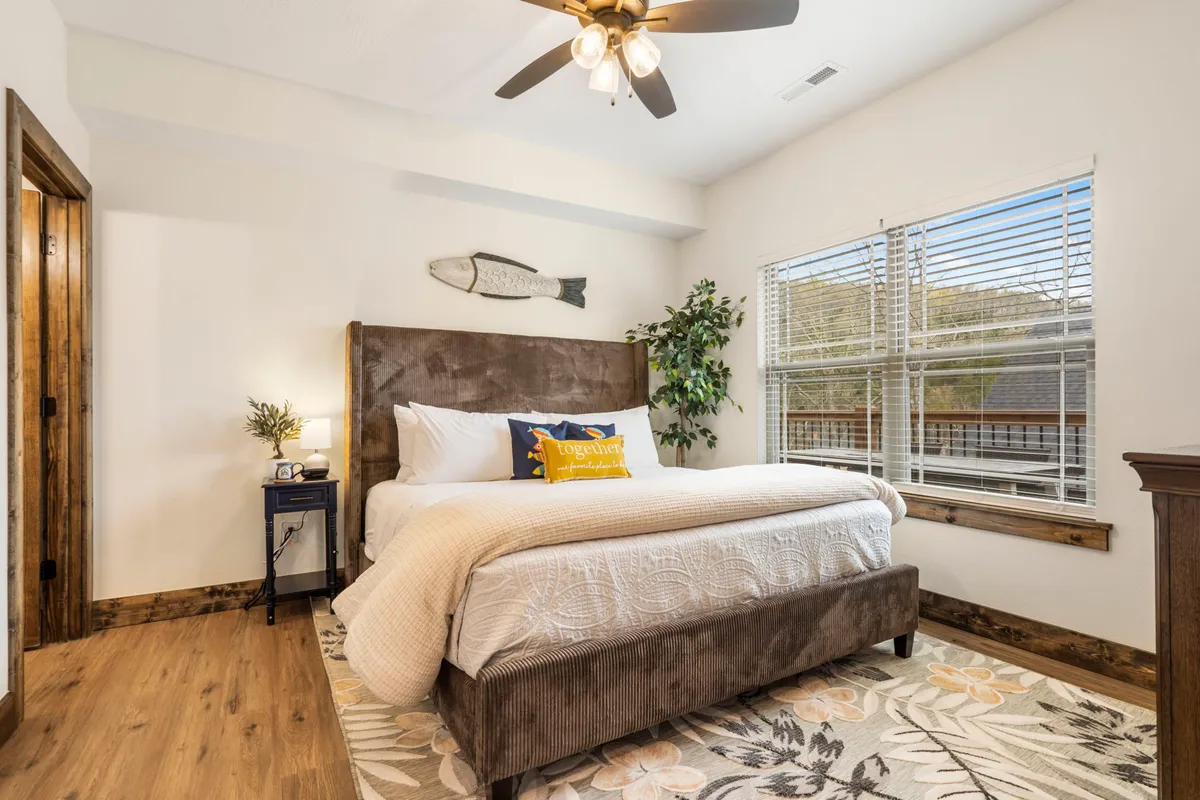 A charming bedroom with a comfortable bed, decorative fish art, window views of the surrounding nature, and a potted plant. The ambiance is peaceful and designed for relaxation, with soft natural light filling the space.