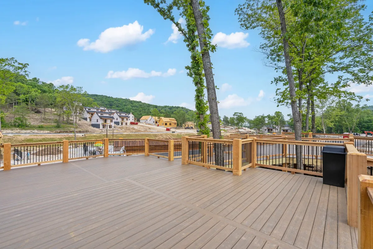 A spacious wooden deck overlooks rolling hills and distant trees, with newly constructed homes in the background. The deck invites relaxation, outdoor dining, and quiet moments shared amid nature’s beauty.