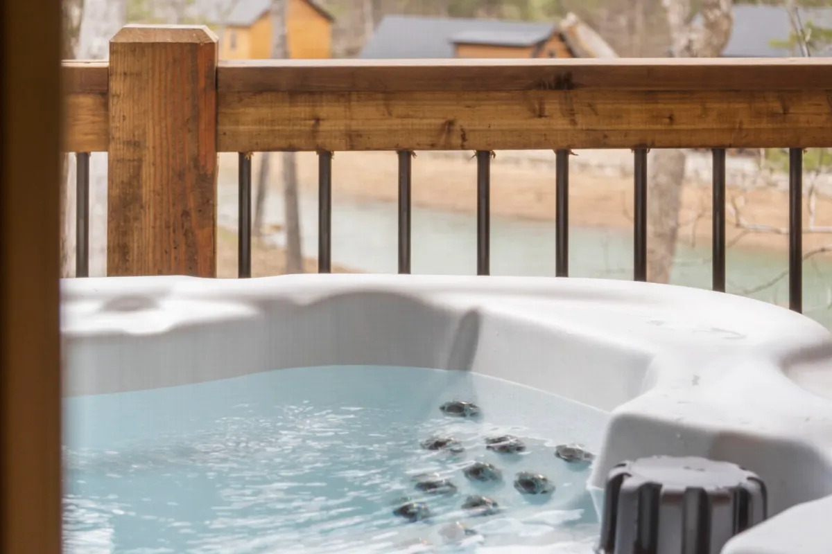 A cozy hot tub perched by a wooden railing, offering a panoramic view of natural Ozark scenery through the trees. The space is tranquil and private, ideal for both morning coffee and stargazing evenings.