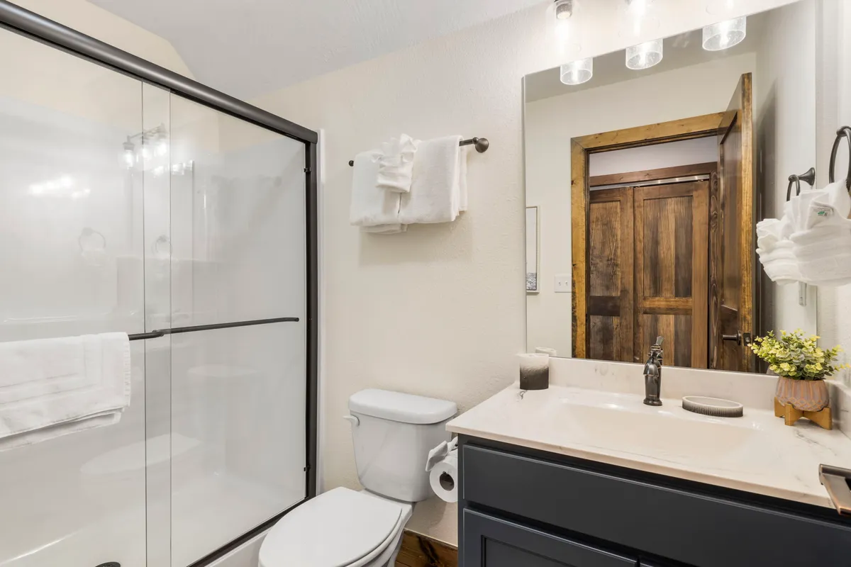 A serene bathroom scene featuring a dedicated shower area, a sink with mirror, and a wooden door, all bathed in tranquil lighting. It's an inviting space for refreshing showers after an adventurous day.