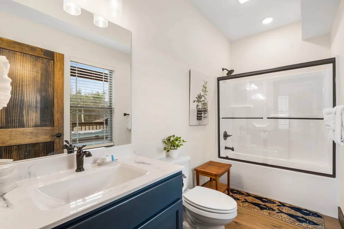 A modern bathroom with dual sink vanity, a large framed shower, framed artwork, and a wooden stool. The space is bright, clean, and calming, designed for soothing morning and evening routines.