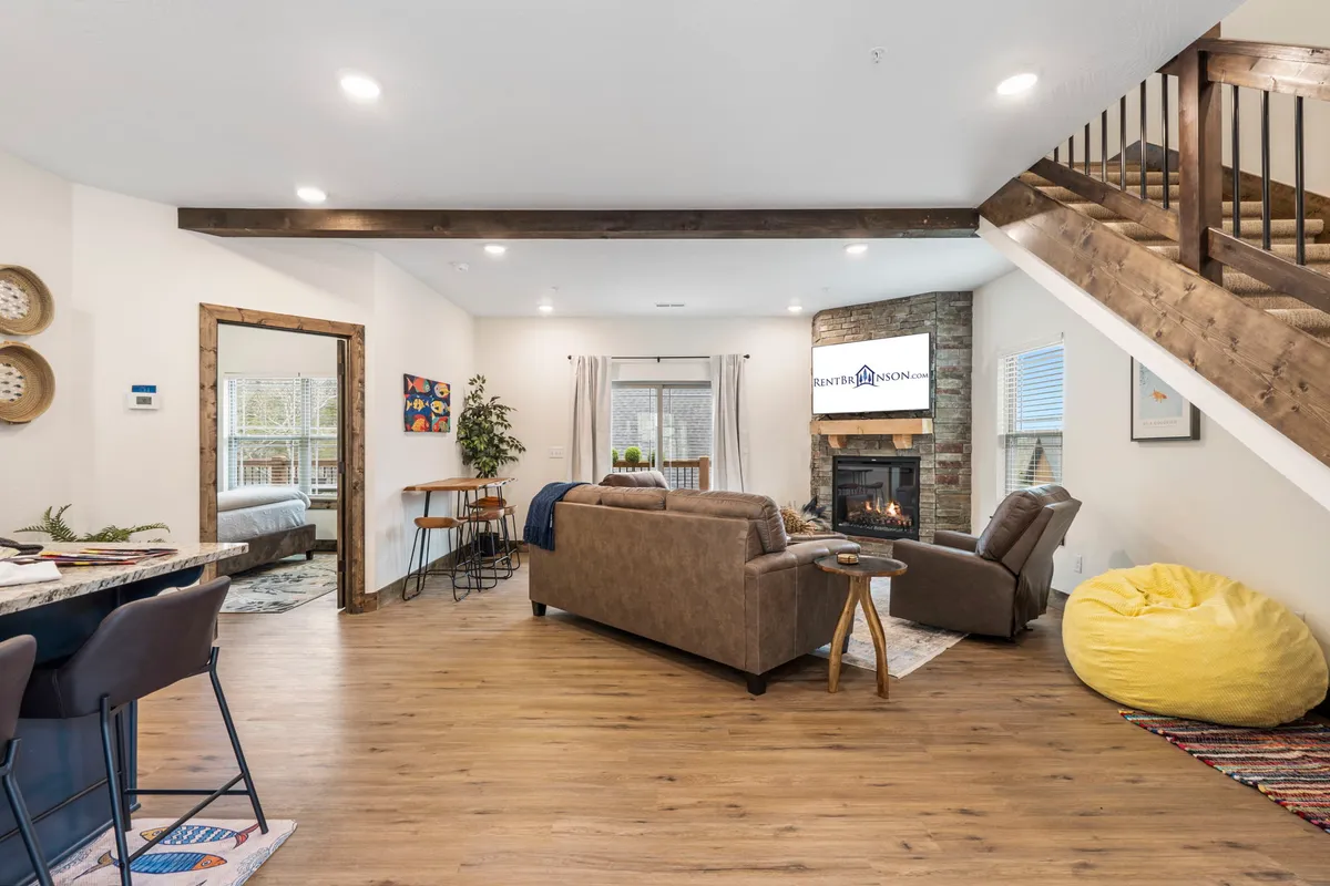 A welcoming interior scene featuring a prominent fireplace as the focal point, accompanied by a comfortable sofa and a staircase in the background. The setup suggests a cozy spot perfect for relaxing, socializing, or enjoying a warm drink by the fire.