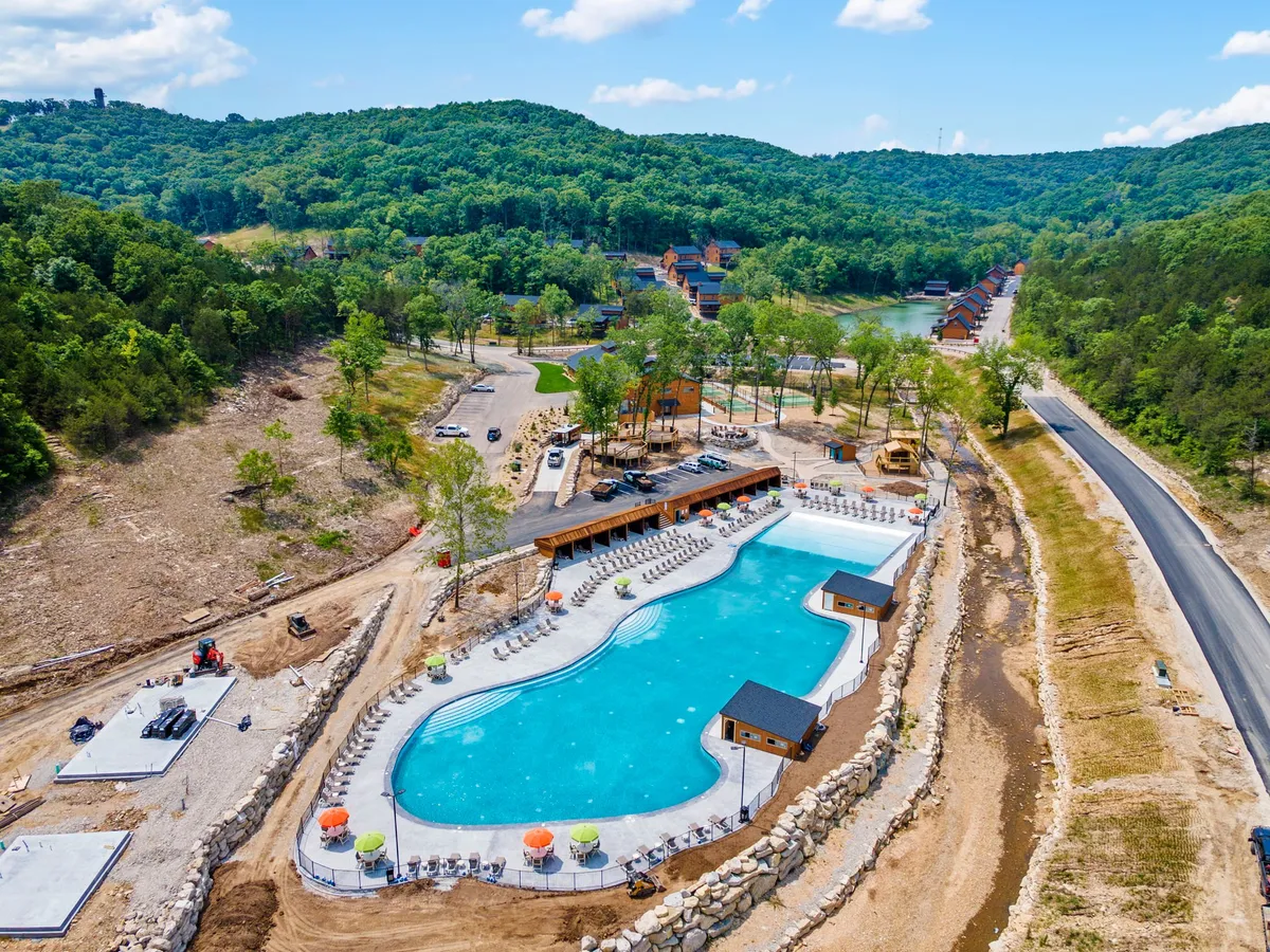 A large outdoor swimming pool surrounded by green hills, poolside lounge chairs, and cabana structures. The area is bright and inviting, suggesting a place for lively gatherings and family fun, with ample space for activities and relaxation.